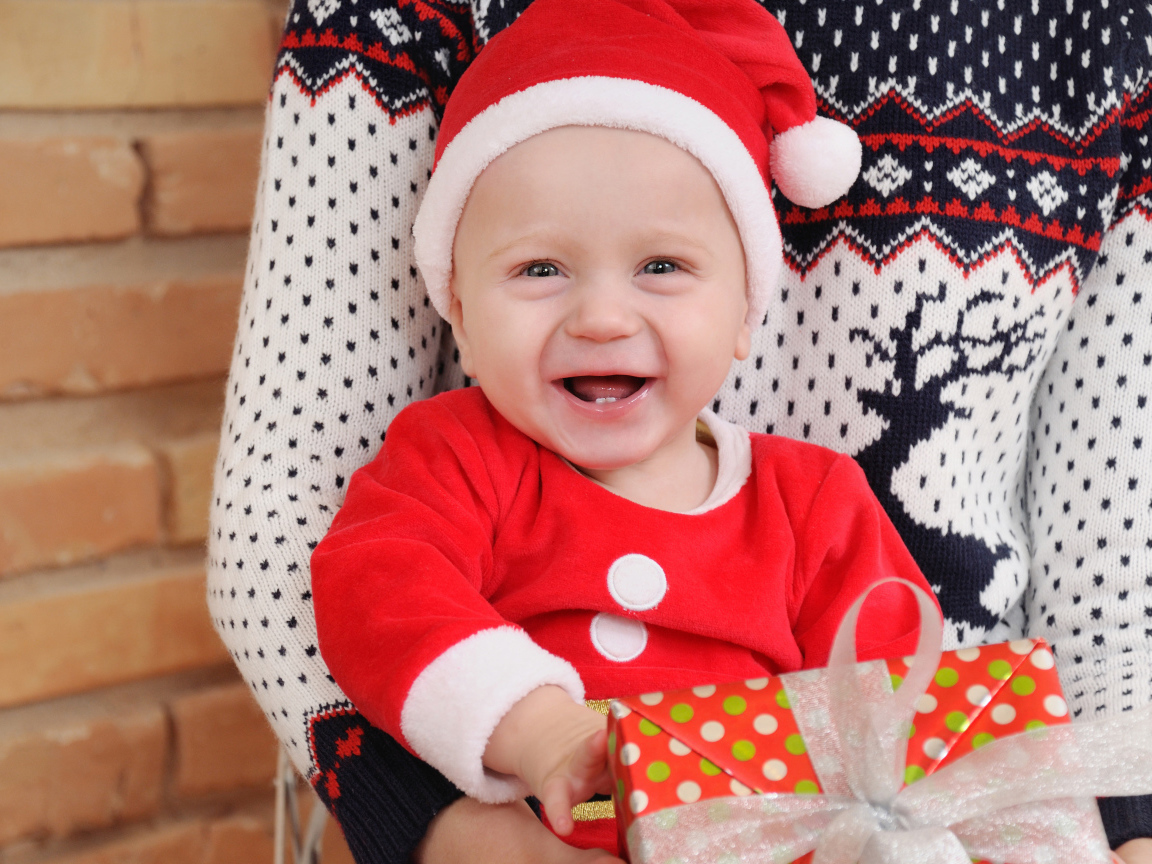 Улыбающийся малыш в костюме с подарком на руках 