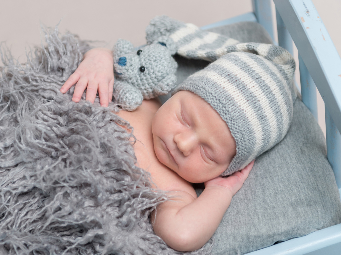 Младенец в вязаной шапке спит с игрушкой под меховым одеялом