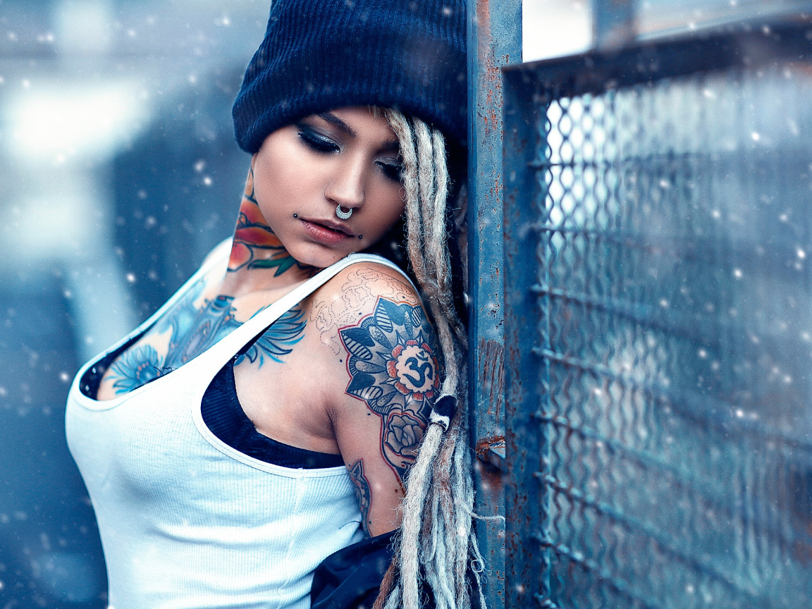 Девушка с татуировками на шее и пирсингом в носу у забора