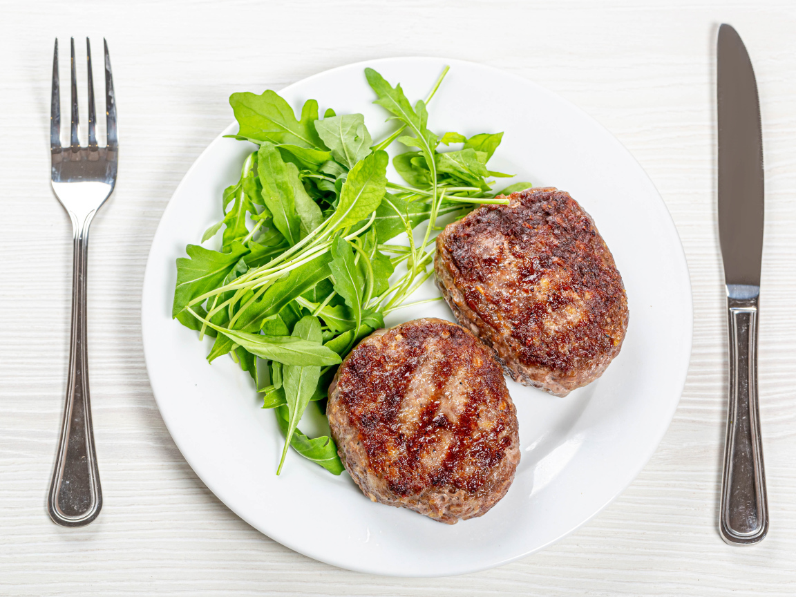 Две котлеты на тарелке с зеленью рукколы 