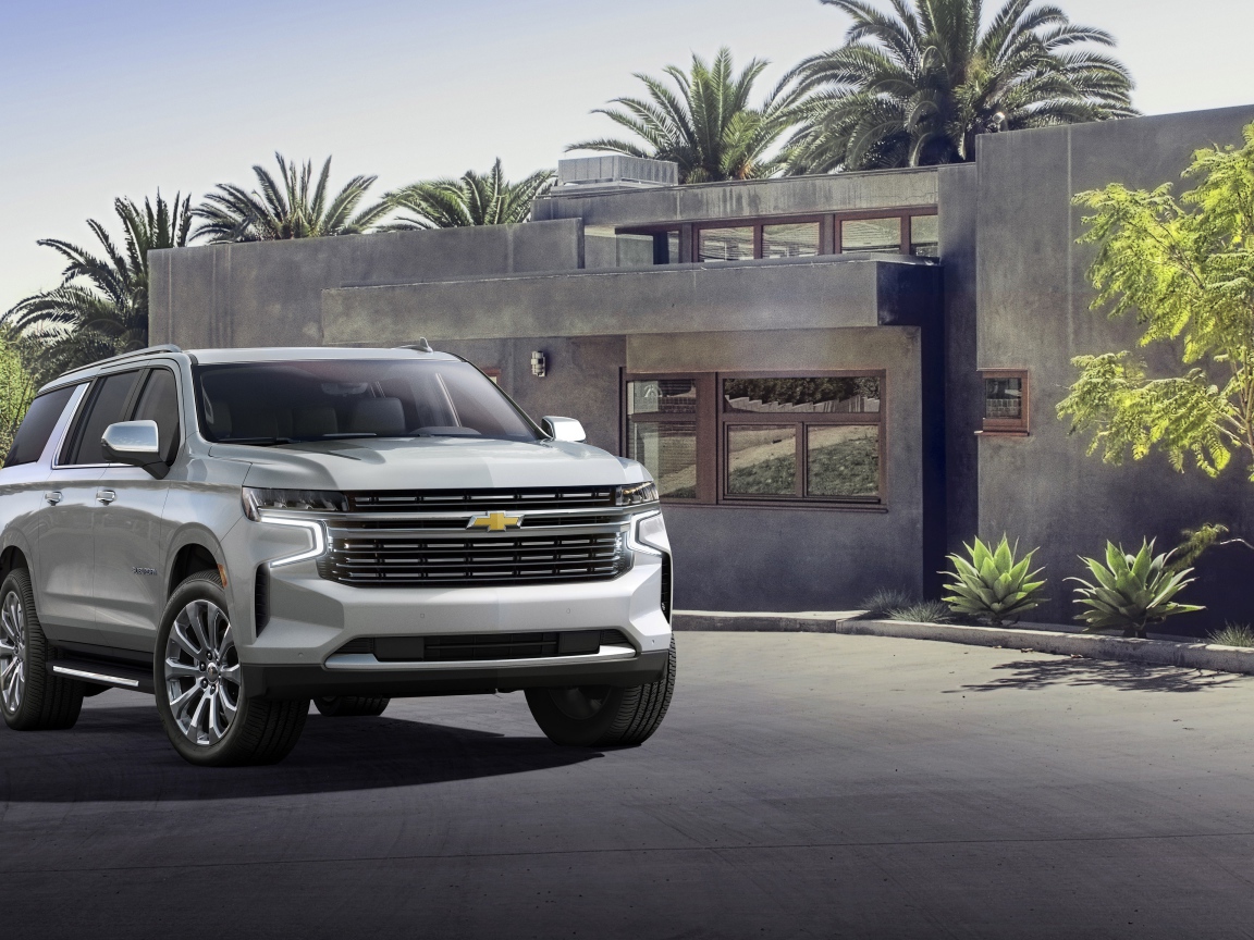 Серый внедорожник Chevrolet Suburban, 2021 года на фоне дома