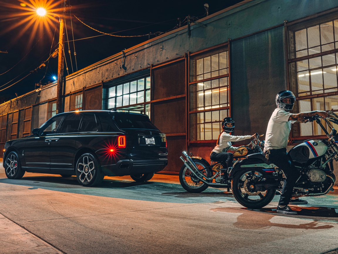 Черный автомобиль Rolls-Royce Cullinan, 2020 года у гаража с байкерами