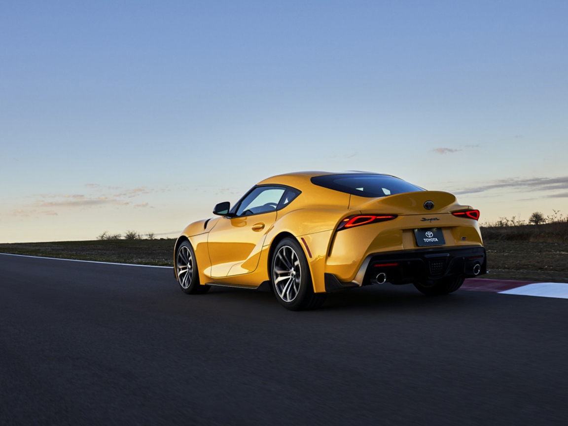 Желтый автомобиль Toyota GR Supra, 2021 года на трассе вид сзади