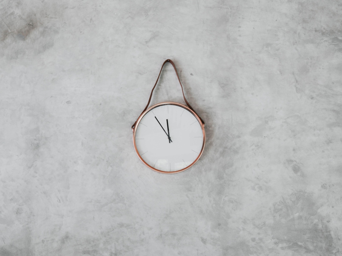 Часы с черными стрелками висят на серой стене 