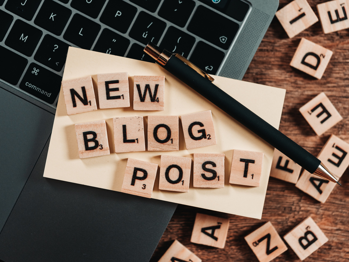 Надпись на английском New Blog Post возле ноутбука с ручкой 