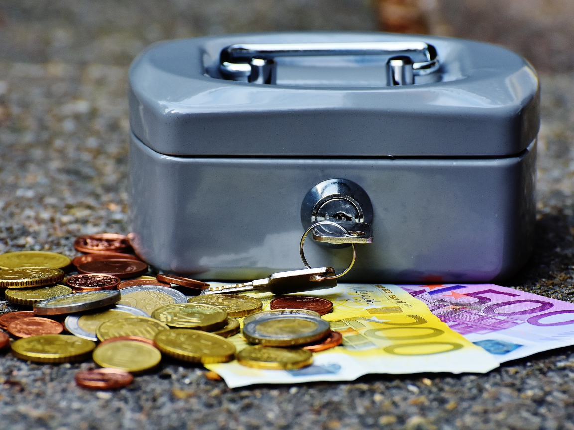 Монеты и купюры на столе с маленьким сейфом