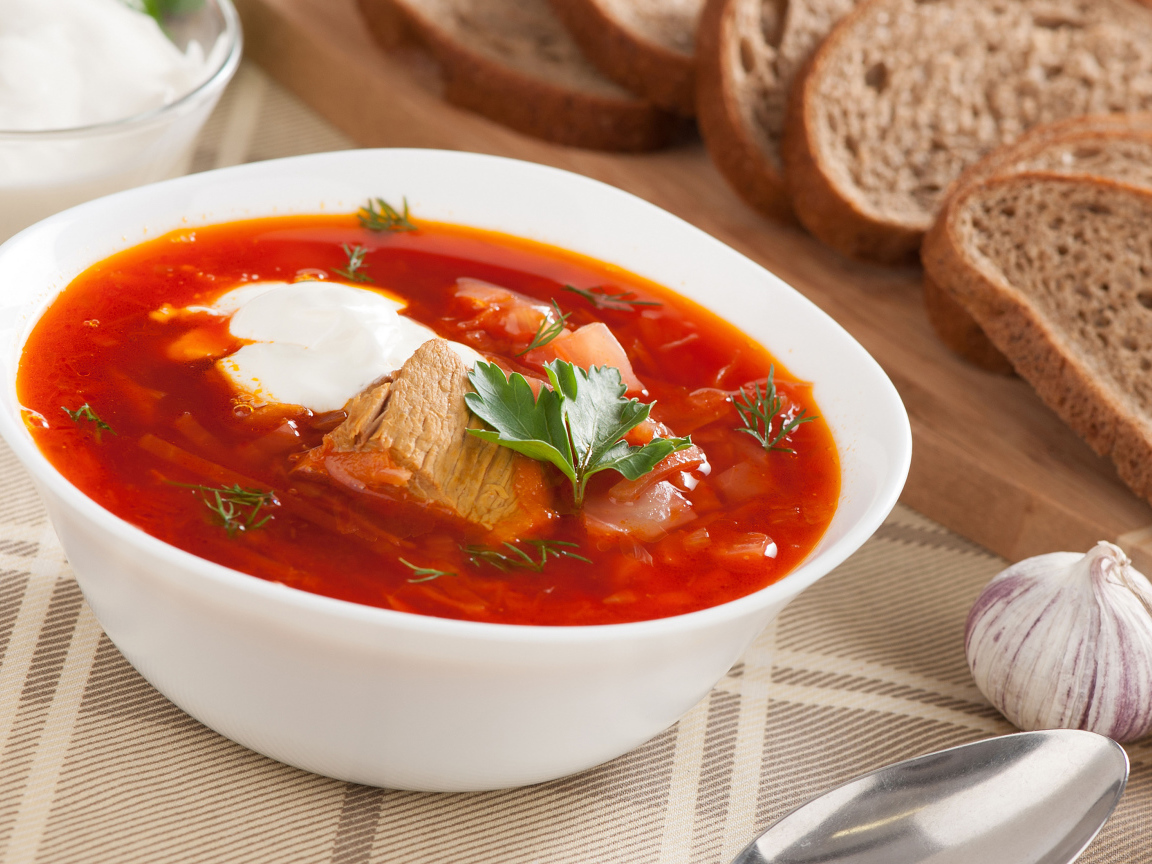 Тарелка горячего борща на столе с хлебом и чесноком