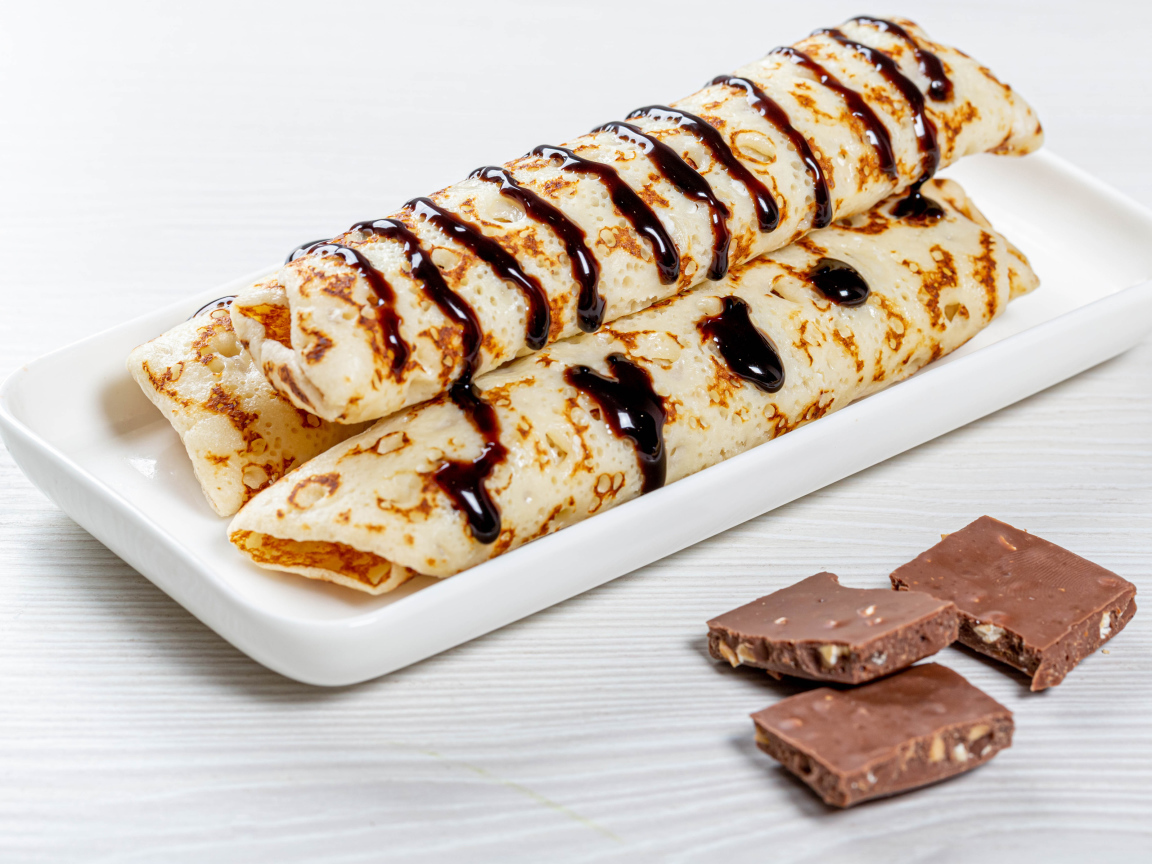 Аппетитные тонкие блины на белой тарелке с шоколадом