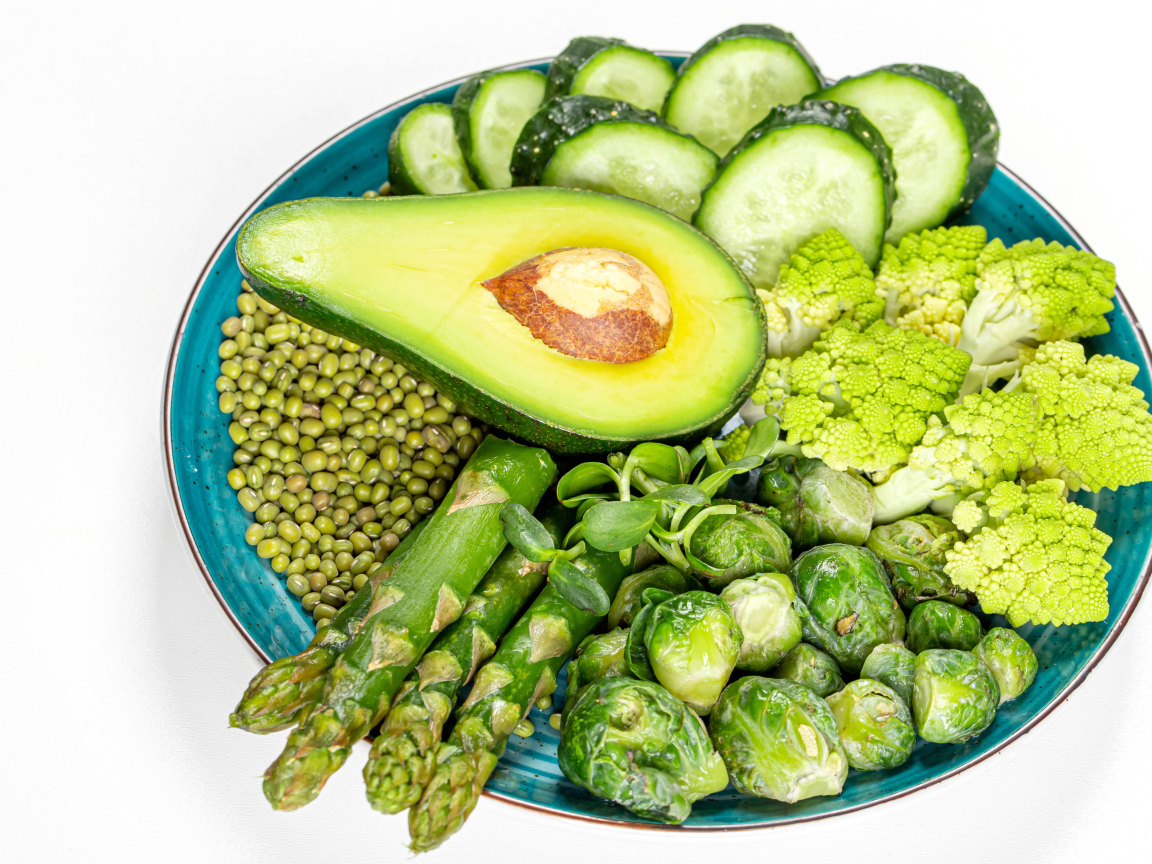 Авокадо, капуста, огурцы и спаржа на тарелке на белом фоне