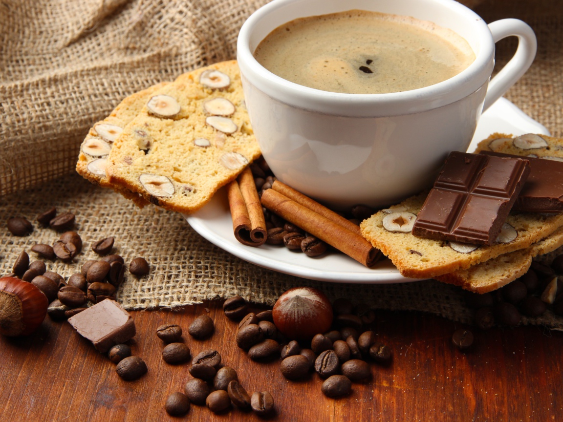 Чашка кофе на тарелке с кексом, шоколадом, корицей и зернами 
