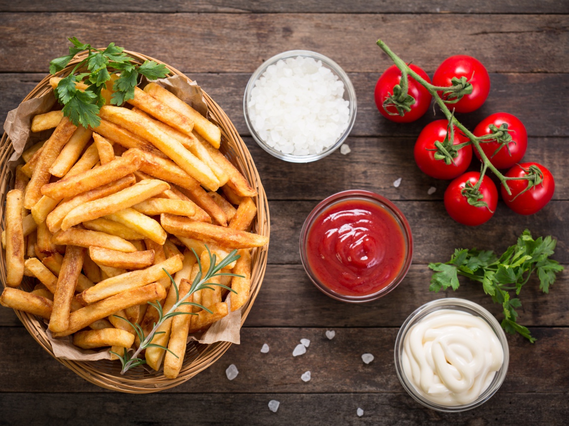 Картофель фри на столе соусом, солью и помидорами 