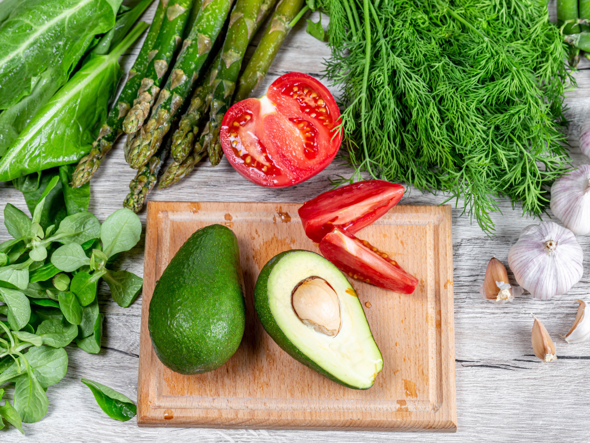 Свежая зелень на столе с авокадо, помидором и чесноком