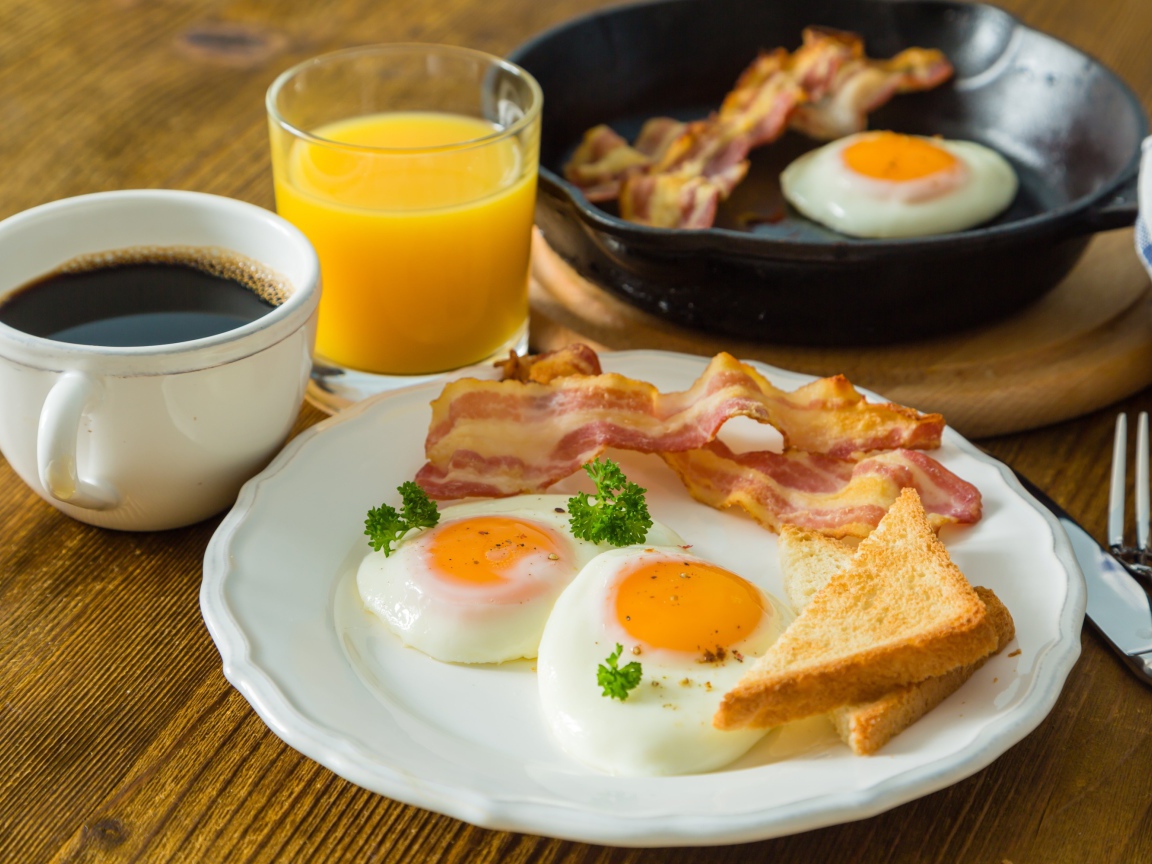 Яичница с беконом и тостами на столе с соком и кофе