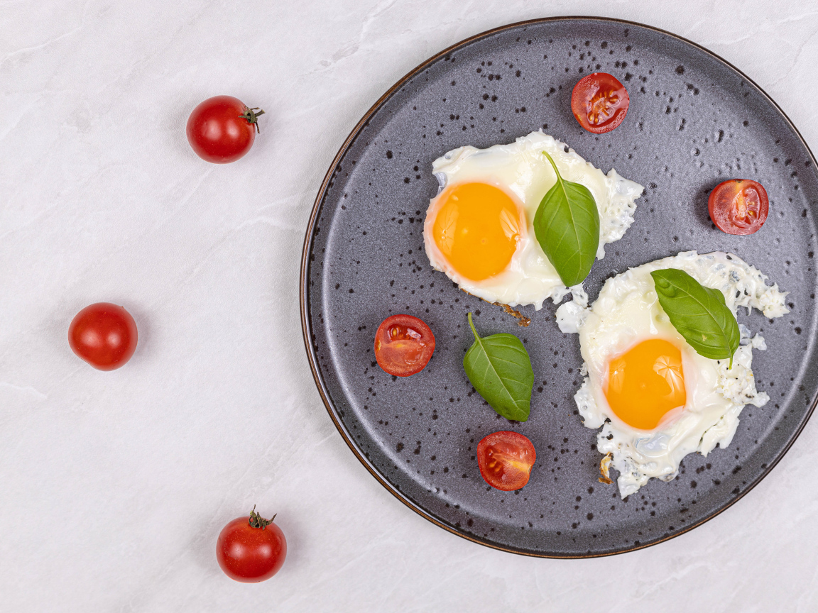 Яичница глазунья с помидорами и листьями базилика на черной тарелке 