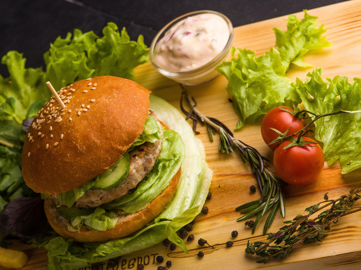 Гамбургер на столе с листьями салата, специями, помидорами и соусом