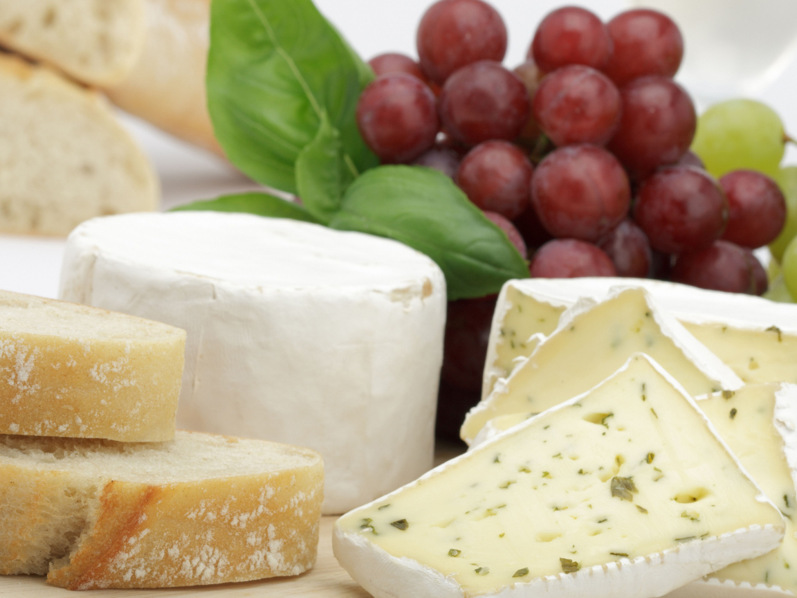 Твердый сыр на столе с батоном и виноградом