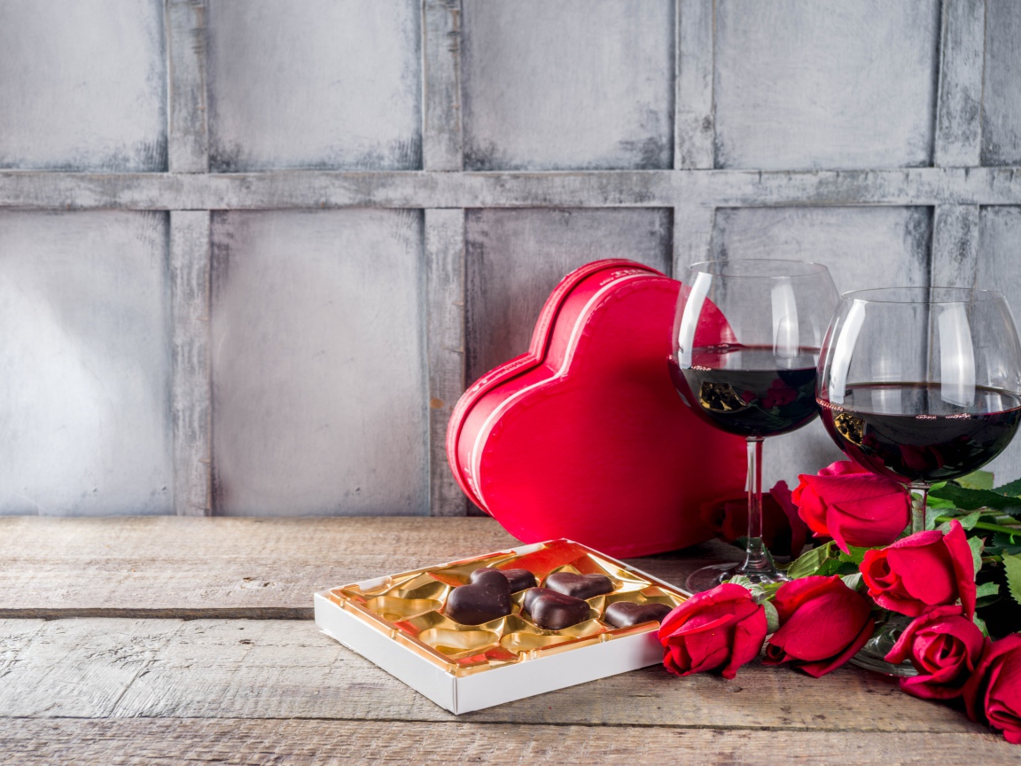 Два бокала вина, шоколадные конфеты и розы на столе для любимой 