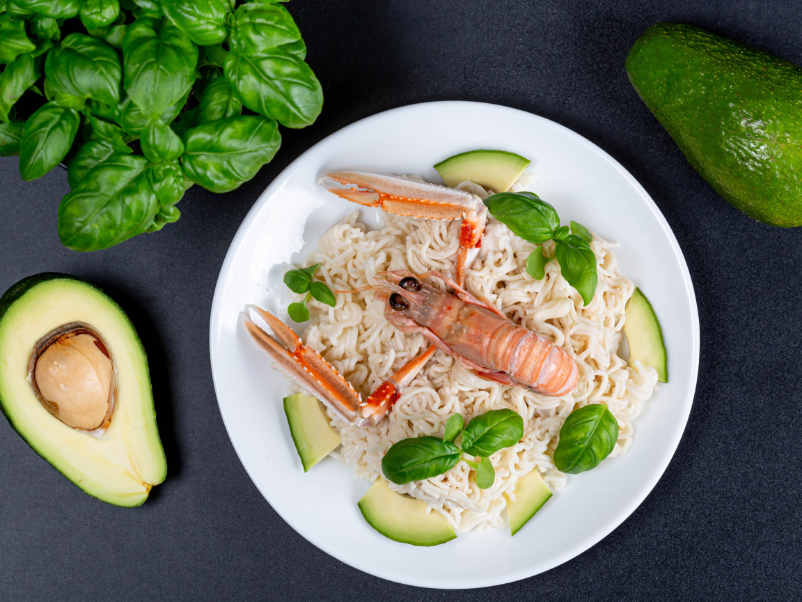 Вермишель с омаром на тарелке с авокадо и листьями базилика 