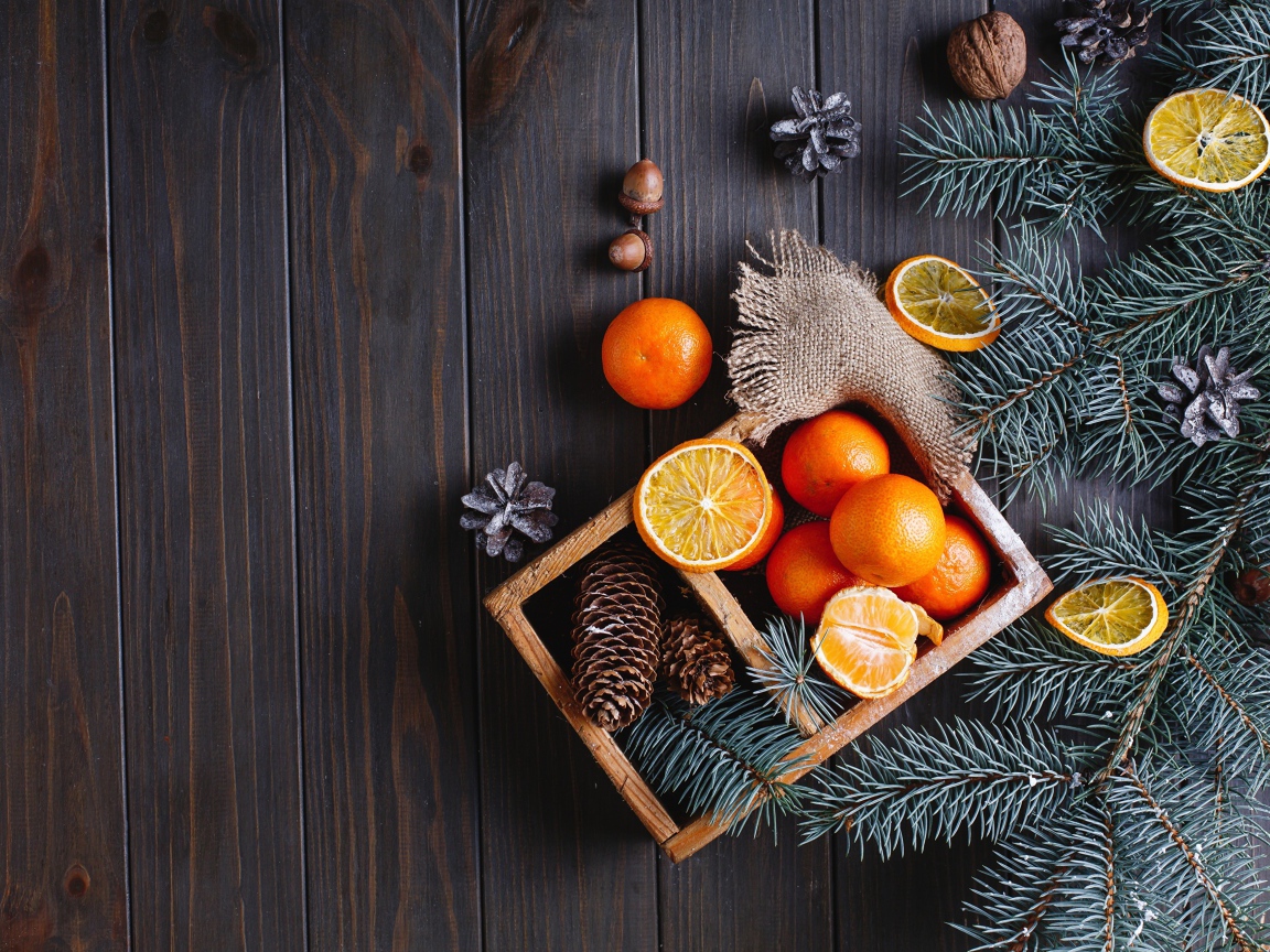 Ящик с мандаринами и шишками на столе с еловыми ветками