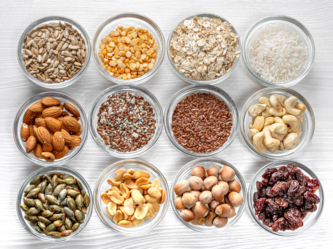 Разные виды орехов, круп и зерен в тарелках вид сверху 