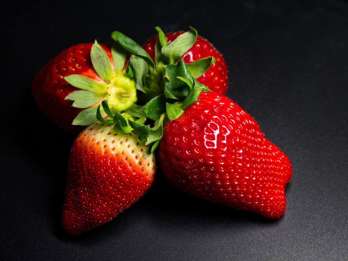 Четыре спелых красных ягоды клубники на черном столе 