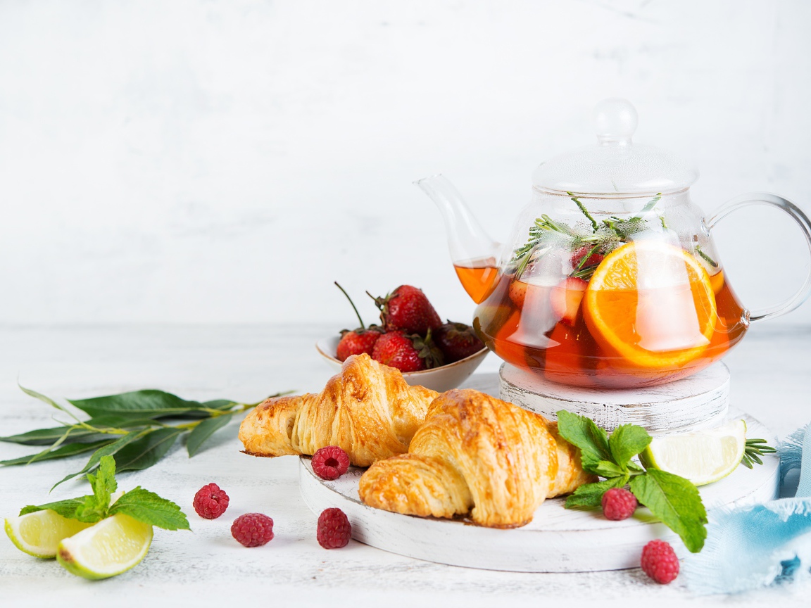 Чайник с лимоном и клубникой на столе с круассанами 