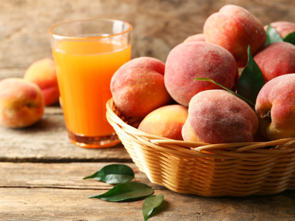 Спелые персики в корзине на столе с соком