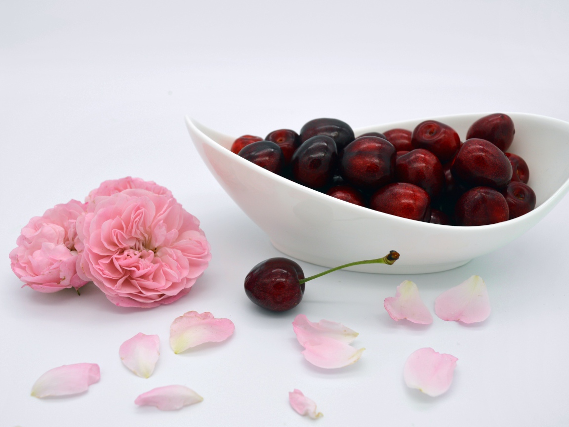 Белая тарелка с красными ягодами черешни на столе с цветами