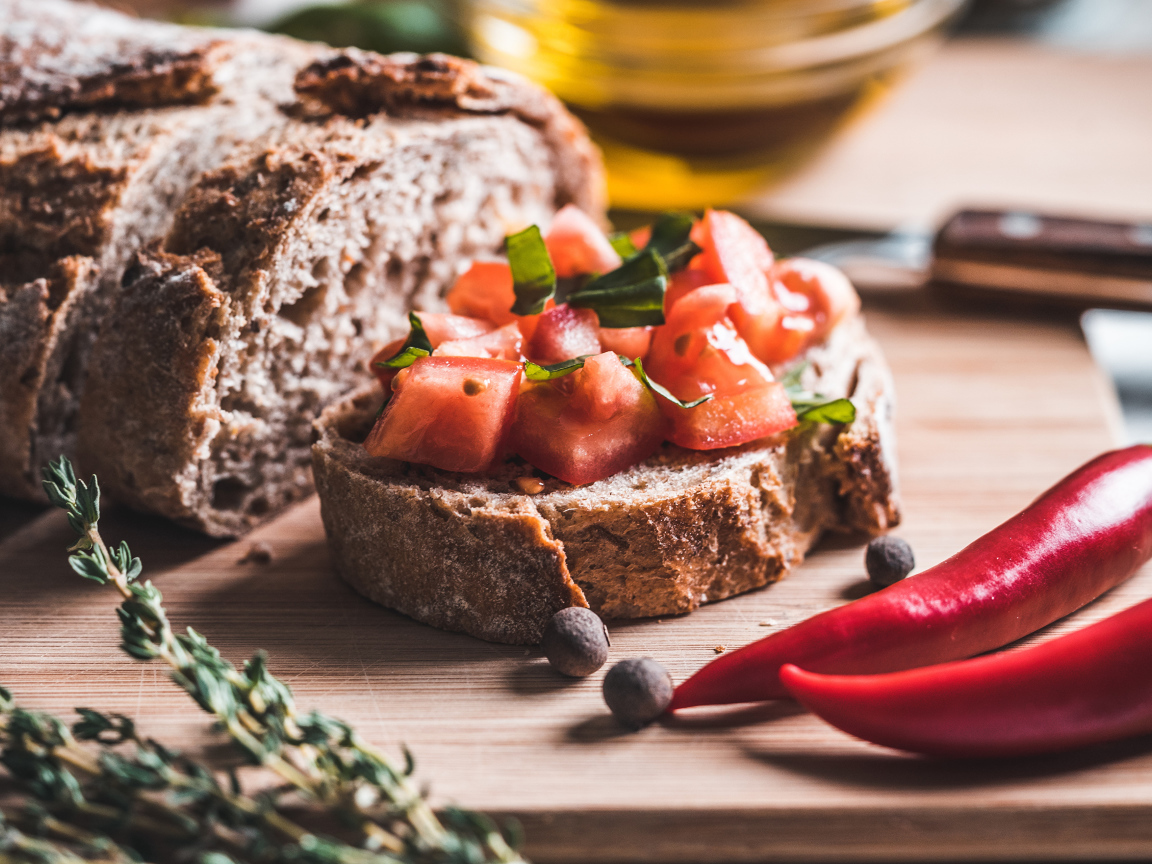 Черный хлеб с кусочками помидора на столе с острым красным перцем