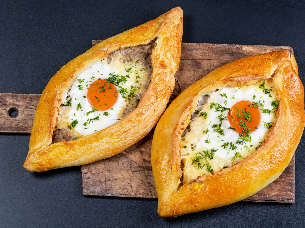 Два больших свежих хачапури с яйцом на доске