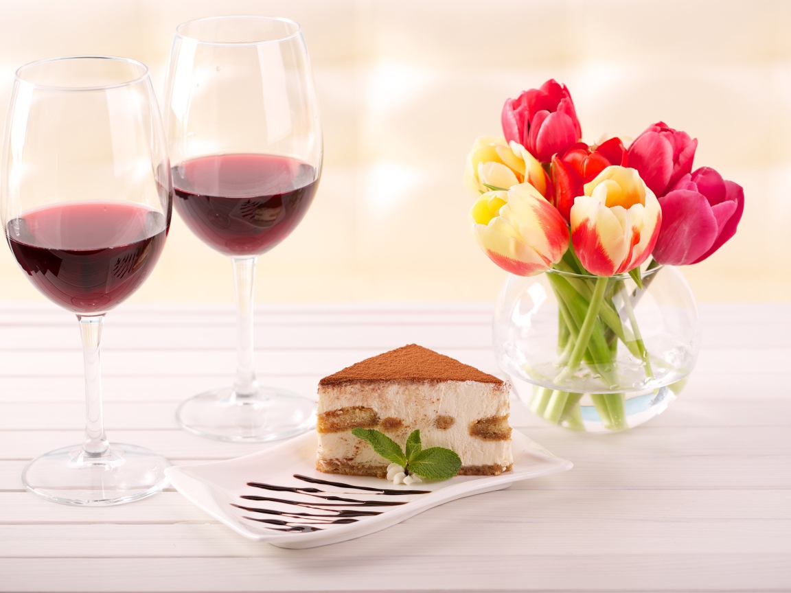 Кусок  тирамису на столе с бокалами вина и букетом тюльпанов