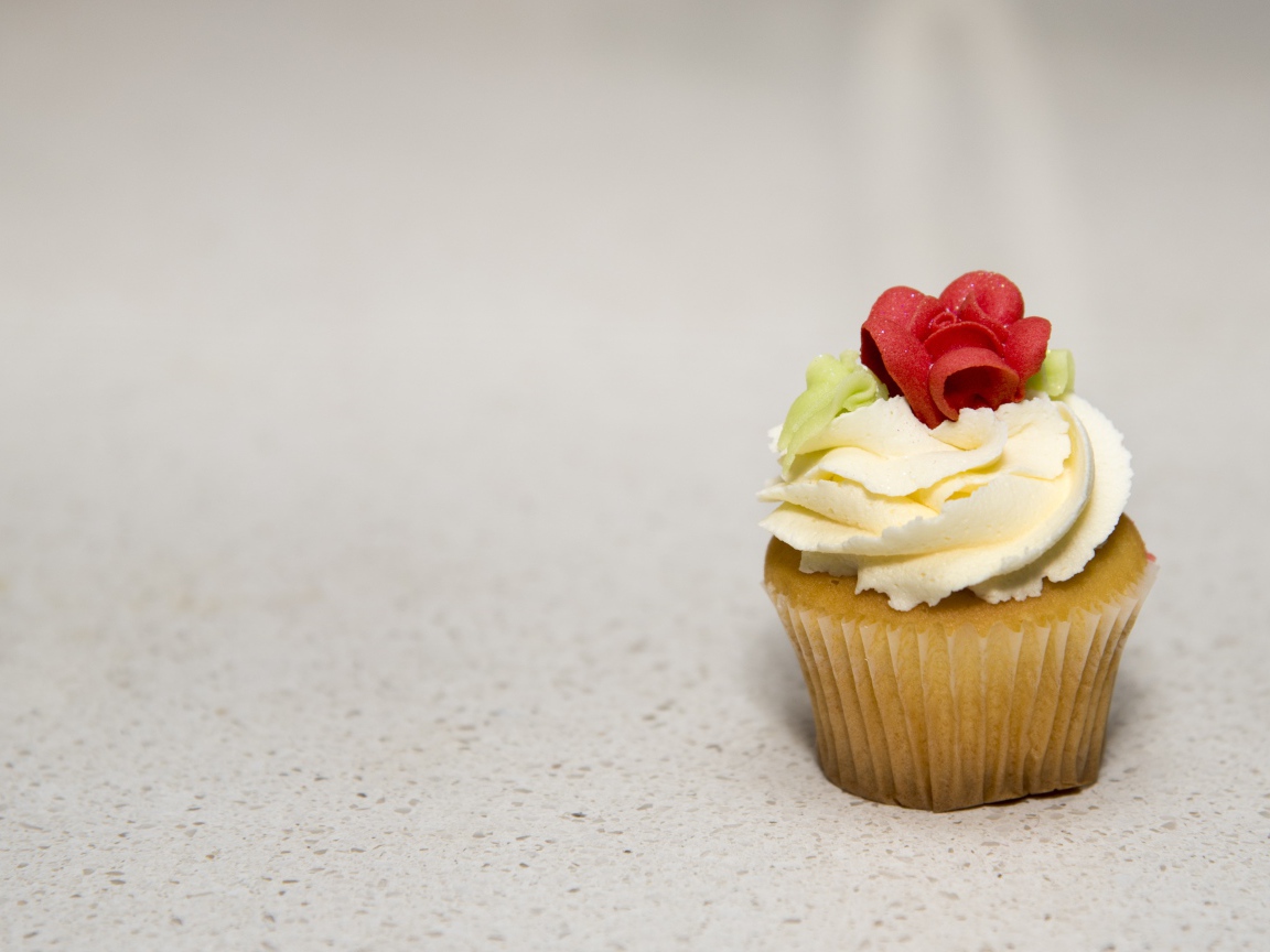 Кекс с кремом и сахарной розой на сером фоне