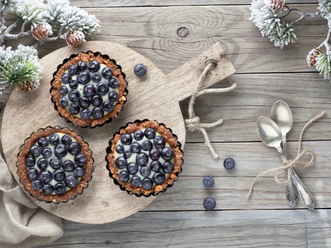 Кексы с кремом и ягодами черники на столе с чайными ложками