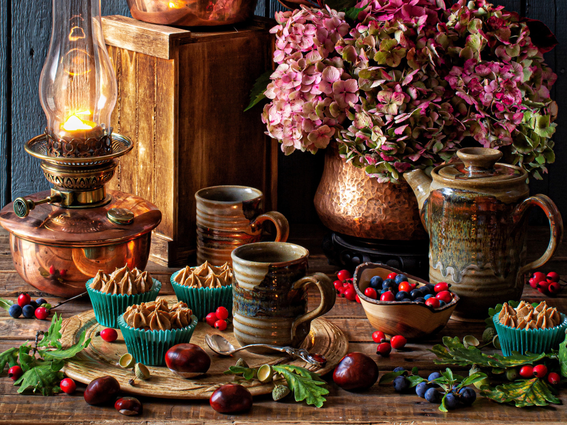 Кексы с кремом на столе с ягодами, цветами и лампой 