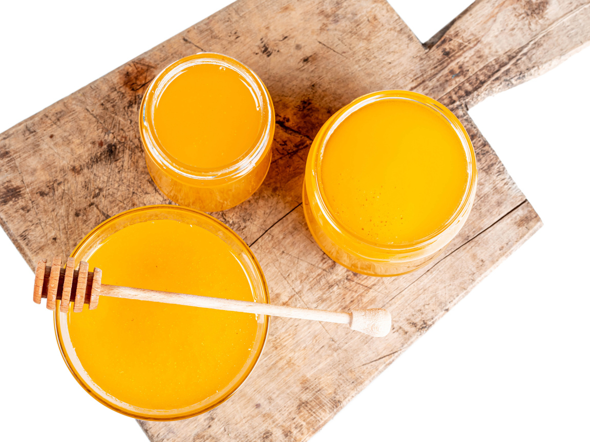 Свежий мед в банках на деревянной доске на белом фоне