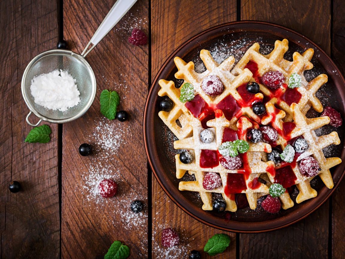 Сладкие медовые вафли на тарелке с ягодами и джемом и сахарной пудрой 