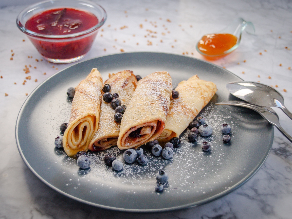 Сладкие тонкие блинчики с ягодами черники на столе с джемом