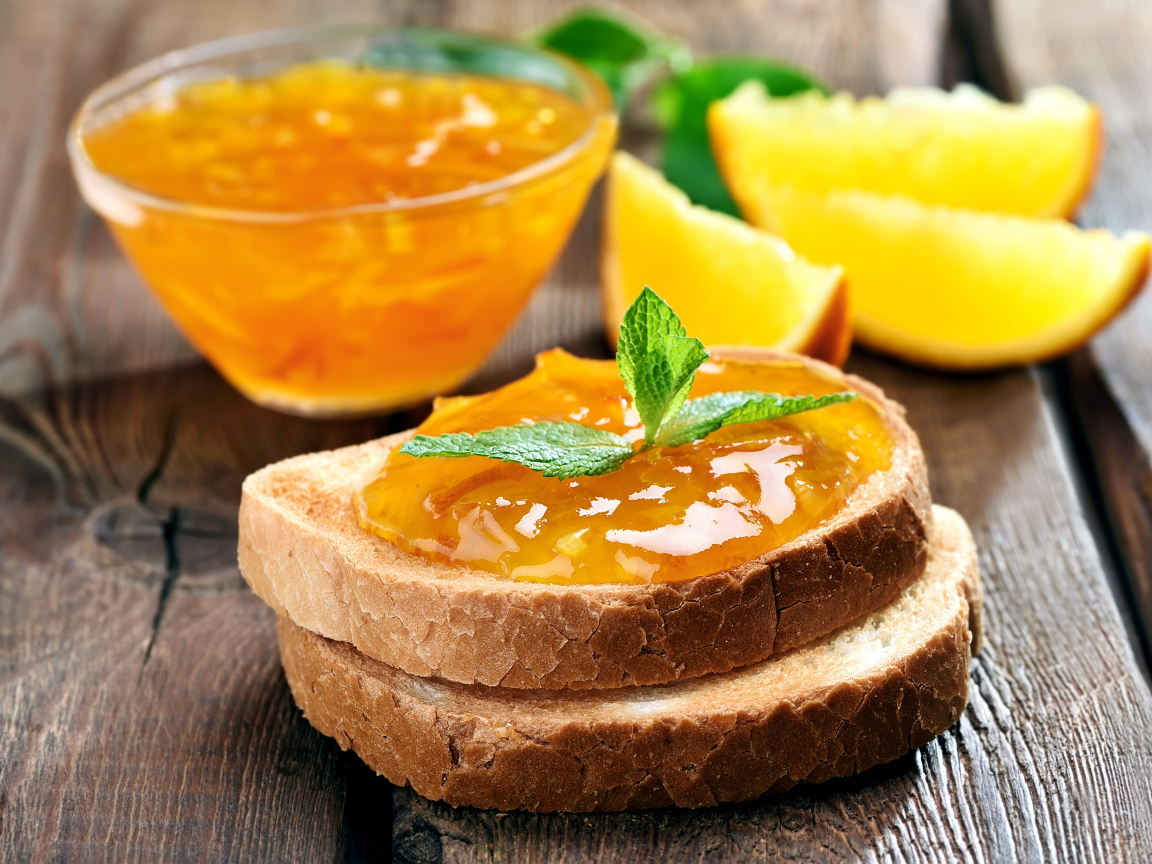 Два кусочка хлеба с апельсиновым джемом на столе с мятой