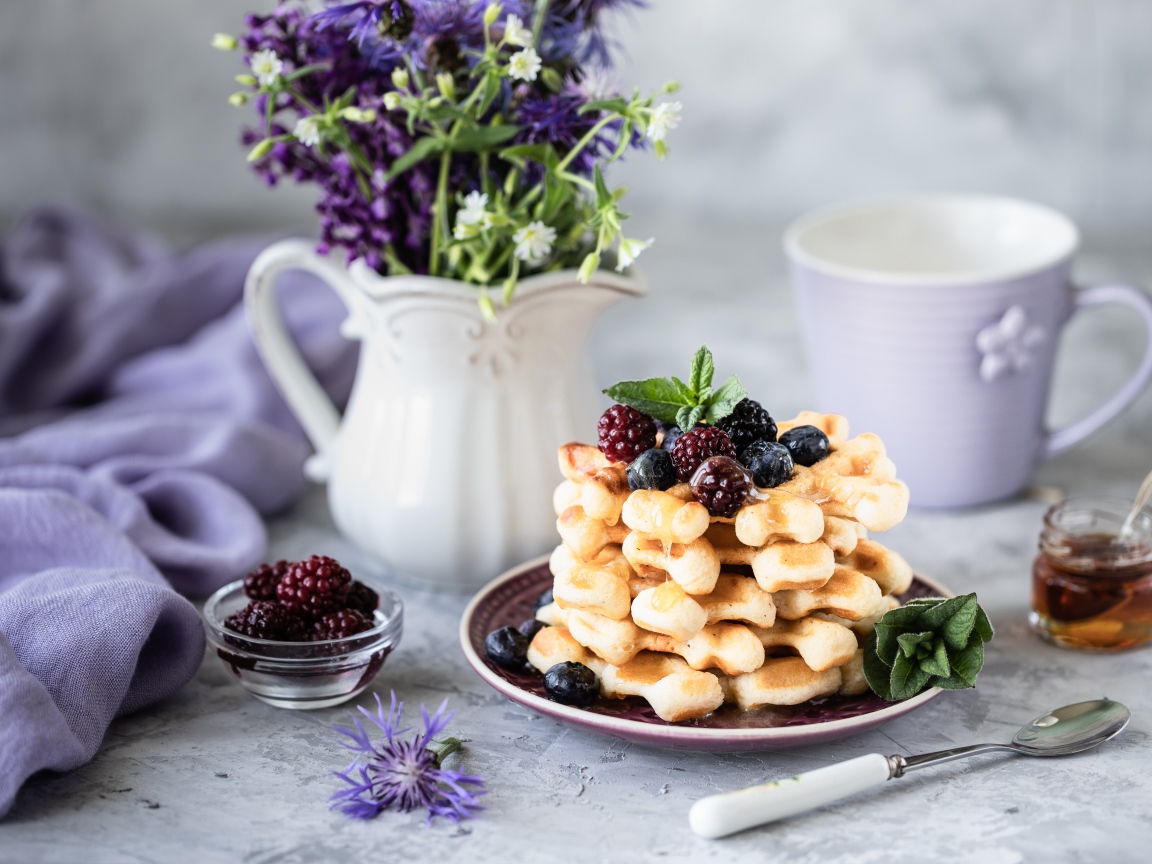 Вафли с ягодами черники и ежевики на столе с букетом