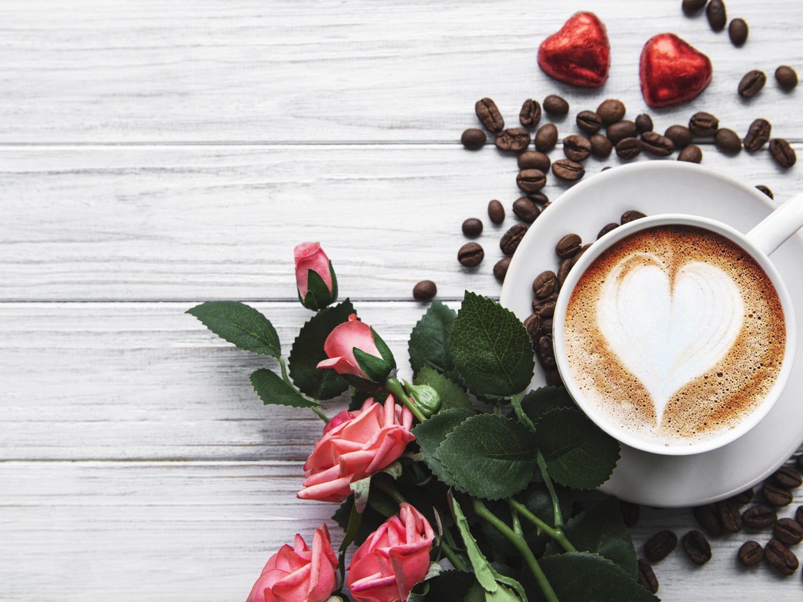 Чашка кофе с рисунком на пене на столе с букетом роз, зернами и конфетами