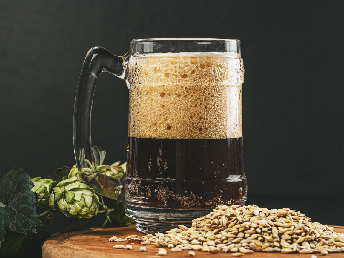 Темное пиво в бокале на столе с хмелем и зернами пшеницы 