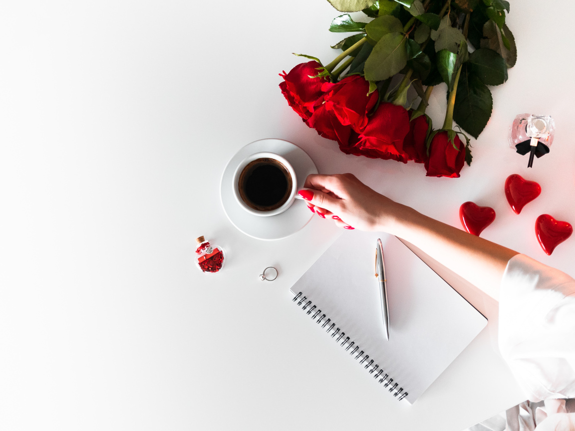 Девушка держит в руках чашку кофе на столе с блокнотом и букетом роз 