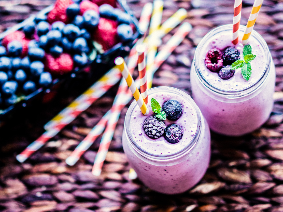 Две банки смузи с трубочками на столе с ягодами
