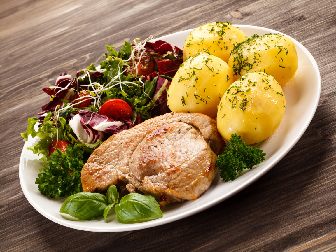 Кусок мяса на тарелке с картофелем и салатом