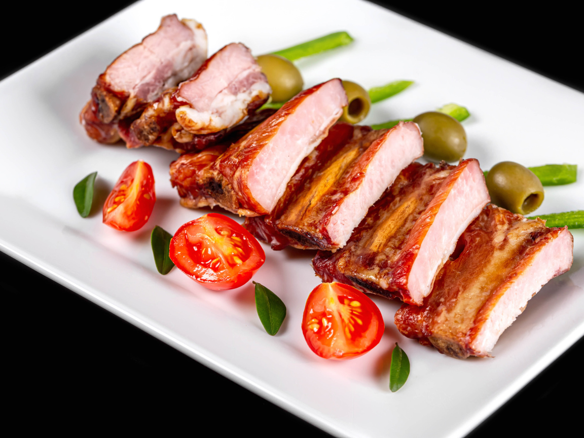 Запеченные ребрышки на белой тарелке с помидорами и оливками