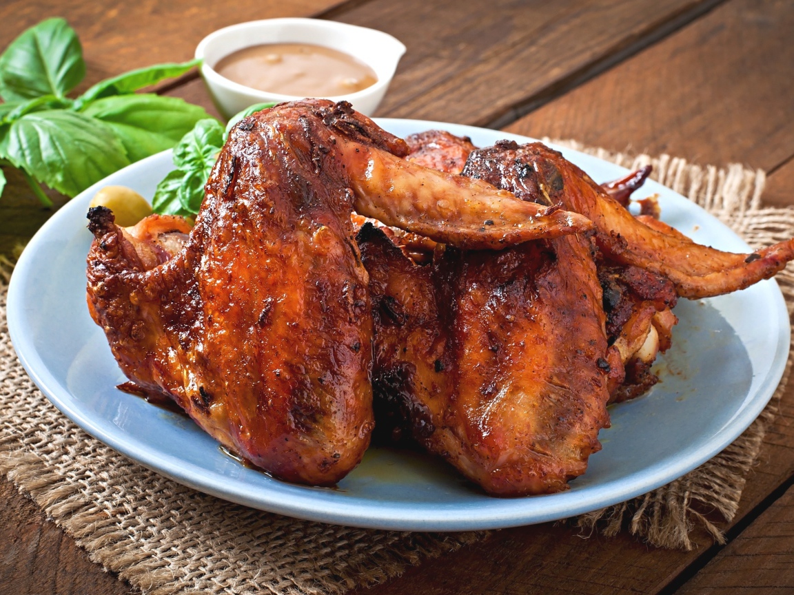 Зажареные куриные крылышки на столе с соусом и базиликом