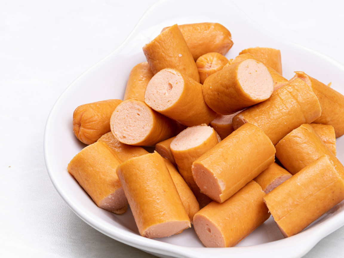 Молочные сосиски кусочками на белом фоне