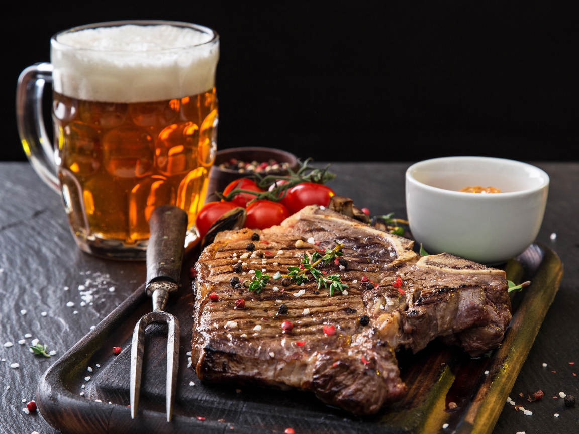 Вкусный кусок мяса на столе с помидорами и бокалом пива