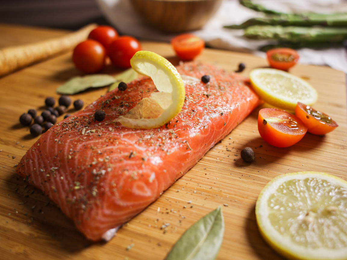 Кусок красной рыбы на доске с лимоном и помидорами