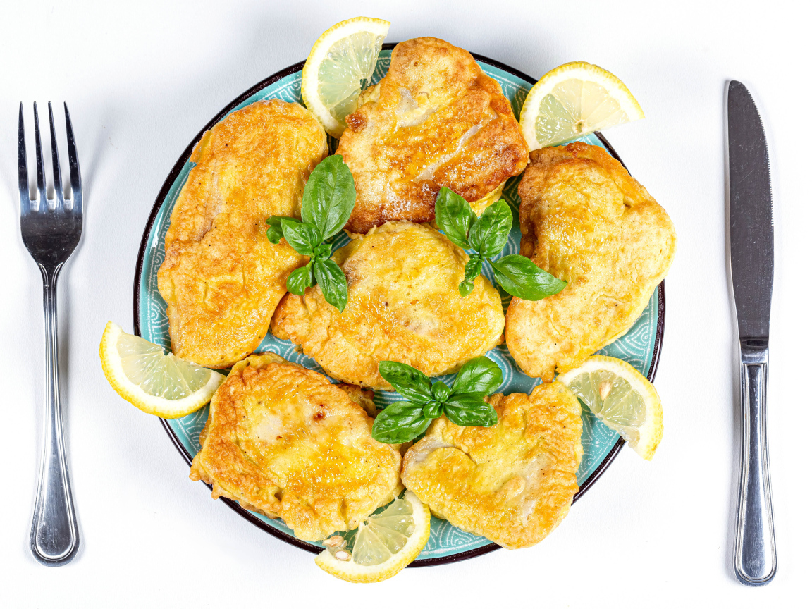 Аппетитная рыба в кляре на тарелке с кусочками лимона и столовыми приборами